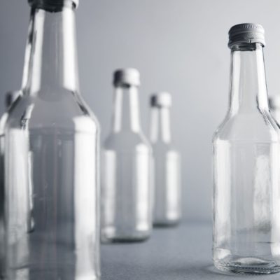 Close view on clear unlabeled empty glass bottles for cold beverages and drinks, randomly presented and isolated on gray background